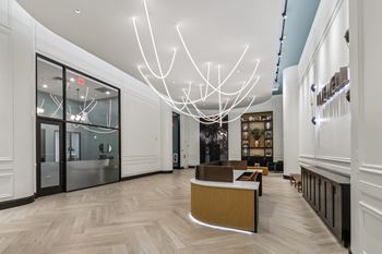 A modern interior with a long hallway, a reception desk, and a large chandelier. at LiveWell Apartments, Pittsburgh, Pennsylvania